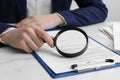 Woman looking at document through magnifier at white marble table, closeup. Searching concept