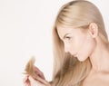 Woman looking at ends of her long blonde hair.