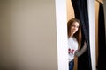 Woman looking out of a changing room door at a clothing store or boutique as she shops for clothes. Copyspace on the