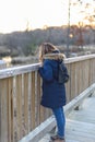 Woman in winter coat peeking over railing of bridge in forest at Royalty Free Stock Photo