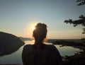 Woman looking over the water standing in the mountains at sunset