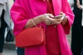 Woman looking at smartphone with red leather bag and fuchsia pink coat before Luisa Beccaria fashion show,