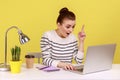 Woman looking surprised by genius idea, raising finger up inspired while working on laptop.