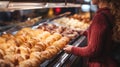 Woman is looking at a variety of pastries displayed in bakery. The display case includes bread, croissants, and other