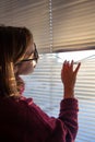 A woman looks through the blinds at the early morning sunlight. Royalty Free Stock Photo