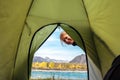 Woman looks inside the green tent and smiles. View from inside tent on the river and mountains on sunny autumn day