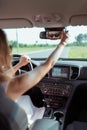 Woman looks in rearview mirror, sits in car in summer in city, reversing, checks children and passengers in back seat of Royalty Free Stock Photo