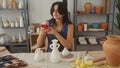 Woman looks at red smartphone by ceramic vase display on pottery worktable in studio; creative concentration Royalty Free Stock Photo