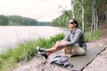 Woman in a loose outfit sitting on the shore of the lake in the summer forest