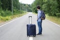 Woman with a luggage standing in the middle of a asphalt road and waiting for a transport