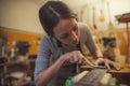 Woman luthier is using a tool to grind a classic guitar fretboard in her musical instrument workshop