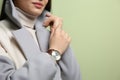 Woman with luxury wristwatch on green, closeup. Space for text