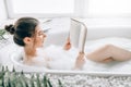 Woman lying in bath with foam and reads magazine