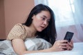 Woman lying on bed while holding cell phone with weird facial expression