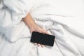 Woman lying on the bed and holding smartphone in hand, Social Addict Concept. Woman sleeping in bed being woken by mobile phone