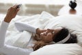 Woman lying in bed listening music using phone and headphones Royalty Free Stock Photo