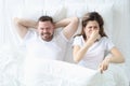 Woman lying in bed with man and covering her nose with her hand