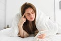 Woman lying in bed in morning, looking confused at smartphone, reading mobile phone with frustrated face, has messy hair Royalty Free Stock Photo