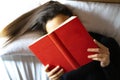 Woman lying in bed reading a red book