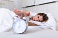 Woman lying in bed turning off an alarm clock in the morning at 7am. Hand turns off the alarm clock waking up at morning, girl Royalty Free Stock Photo