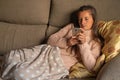 Woman lying on the sofa and covered with a blanket looks serious at her mobile phone Royalty Free Stock Photo