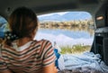 Woman lying in the cozy car trunk and enjoying the mountain lake view in the morning after the camper night. Warm early autumn