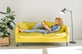 Woman lying on cozy yellow couch and reading book Royalty Free Stock Photo