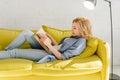 Woman lying on cozy yellow couch and reading book Royalty Free Stock Photo