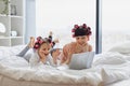 Woman lying with a cute girl on the bed, curling their hair, using a laptop. Royalty Free Stock Photo