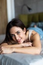 Young woman lying at the end of the bed underneath the quilt and smiling, with her head resting upon her hand with the other in Royalty Free Stock Photo