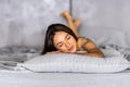 Young woman lying at the end of the bed underneath the quilt and smiling, with her head resting upon her hand with the other in Royalty Free Stock Photo