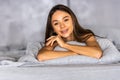 Young woman lying at the end of the bed underneath the quilt and smiling, with her head resting upon her hand with the other in Royalty Free Stock Photo