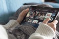 Woman lying on sofa with blanket and choosing a netflix movie on tablet