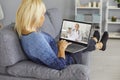 Woman lying on sofa and communicating with smiling woman therapist online on laptop