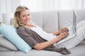 Woman lying on sofa using her laptop smiling at camera Royalty Free Stock Photo