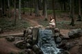 A woman in a macrame dress is sitting on a large fountain in a green forest.