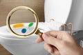 Woman with magnifying glass detecting microbes on toilet bowl in bathroom