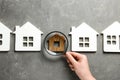 Woman with magnifying glass exploring different house models on grey stone background. Search concept