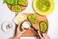 Woman makes a homemade avocado sandwich. White table with a plate of mashed avocado, spices, and a box of cream cheese. Cooking Royalty Free Stock Photo