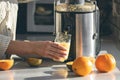 A woman makes orange juice at home in the kitchen with an electric juicer.