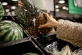 Woman makes purchases in department of vegetables, fruits in store. Hand holds pineapple selection of products. Diet. Vitamins and