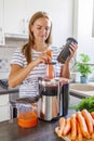 A woman making carrot juice from fresh carrots with a home juicer in the kitchen Royalty Free Stock Photo