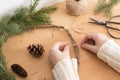 Woman making a christmas wreath with firs and cones on a wooden table