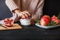 Woman making fresh pomegranate juice using hand juicer near ingredients on black wooden background.