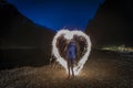Woman making a heart shape with a sparkler at night with towering cliffs in the background o