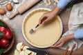 Woman making holes in raw dough with fork at table, top view. Baking apple pie