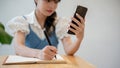 A woman making lists in her notebook while using her smartphone, sitting at a table indoors Royalty Free Stock Photo