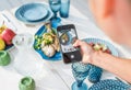 Woman making photo using smartphone Grilled fish in the oven and served on a white wooden table with vegetable salad and fruits. Royalty Free Stock Photo