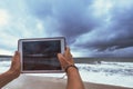 Woman making photo using tablet pc of storm seashore during vacation on Bali