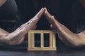 Woman making roof with her hands on wooden cube house protecting her property and investment. Wooden house dark background